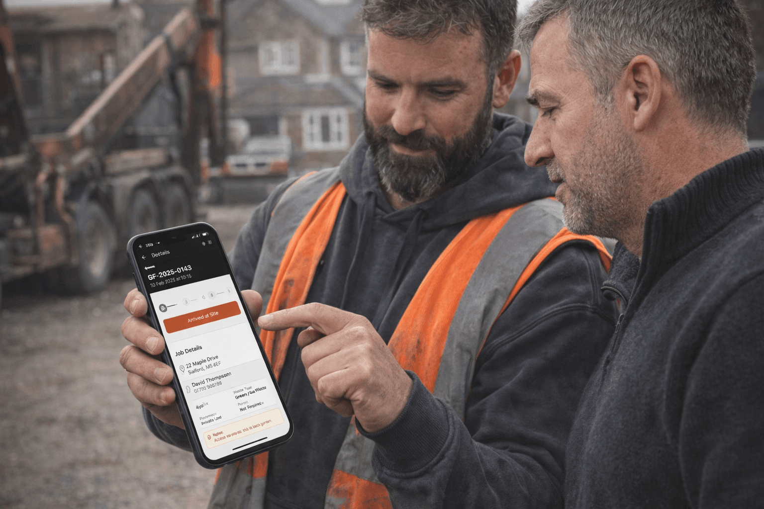 Two skip hire workers viewing job details on a phone on-site